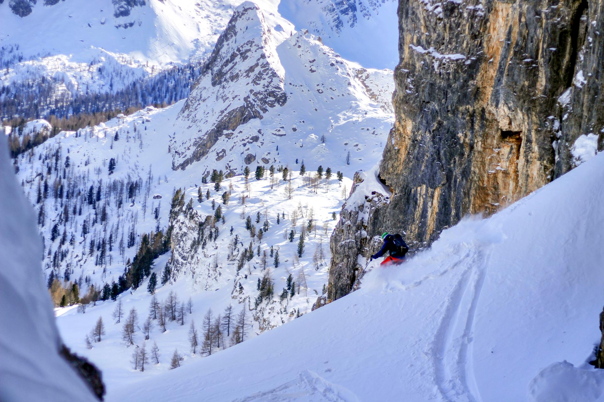 Skiier skiing down off piste slope between rocky mountain faces
